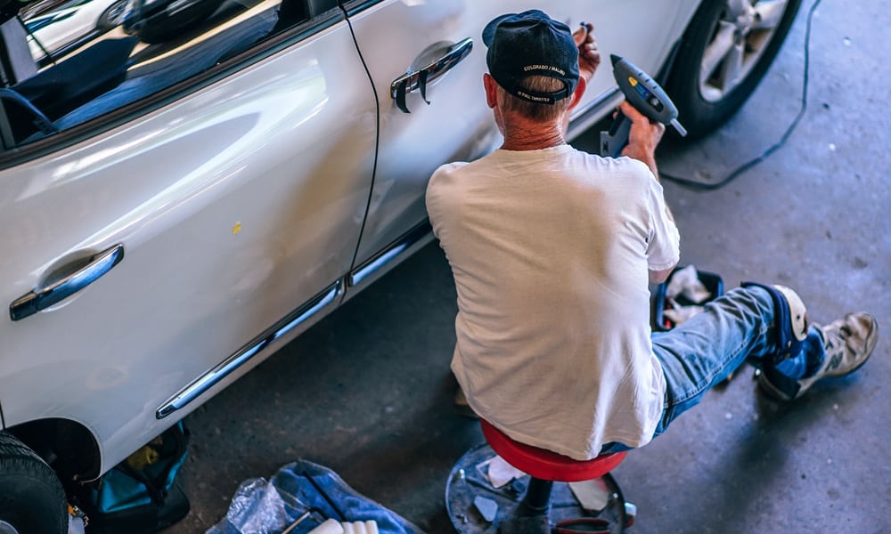 A man using hot glue gun on a car